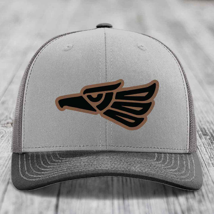 Grey trucker hat with black and brown Aztec eagle leather patch on front.