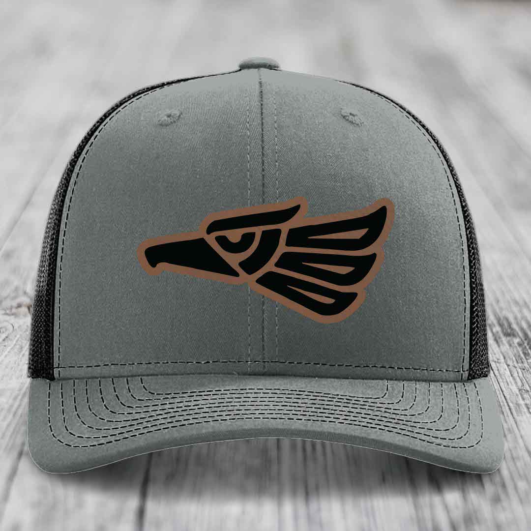 Grey trucker hat with black and brown Aztec eagle leather patch on front.