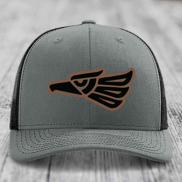 Grey trucker hat with black and brown Aztec eagle leather patch on front.