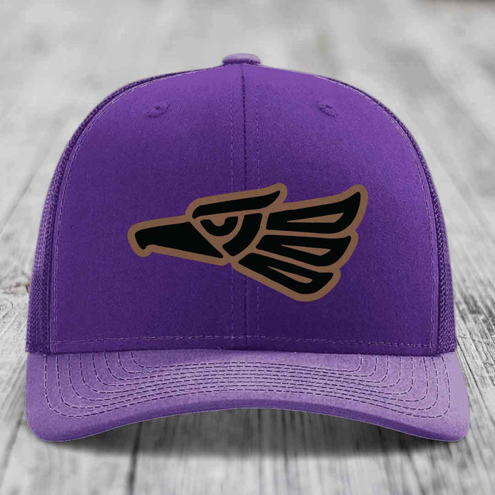 Purple trucker hat with black and brown Aztec eagle patch on front.