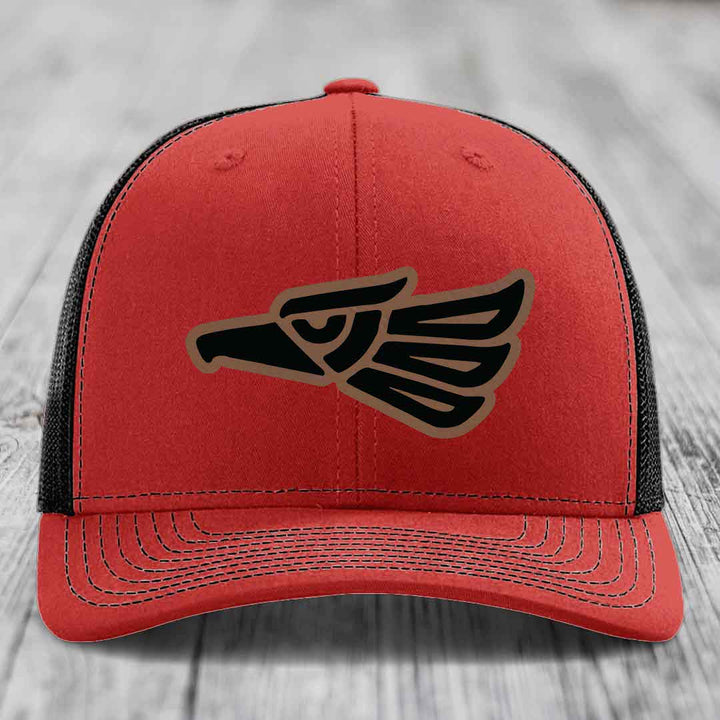 Red trucker hat with black and tan Aztec eagle patch on front.