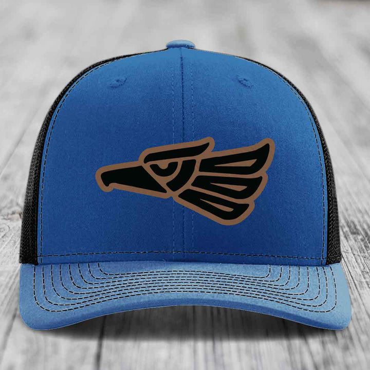 Blue trucker hat with black and brown Aztec eagle patch on front.