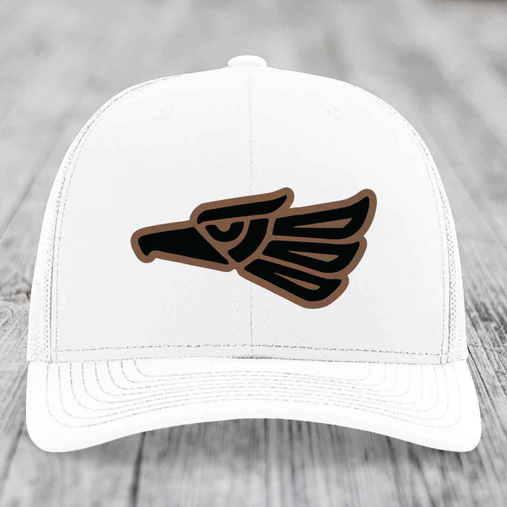White trucker hat with black and brown Aztec eagle leather patch on front.