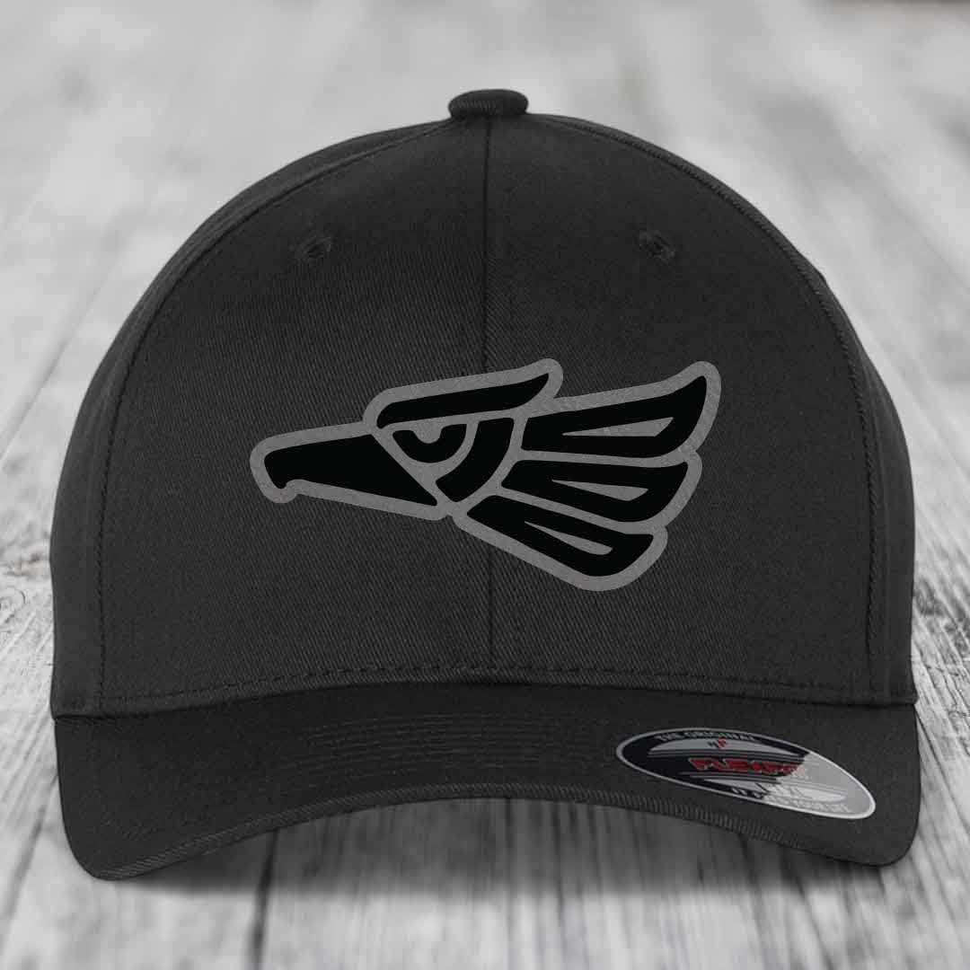 Black baseball cap with Aztec-style eagle patch on front, displayed on wooden surface.
