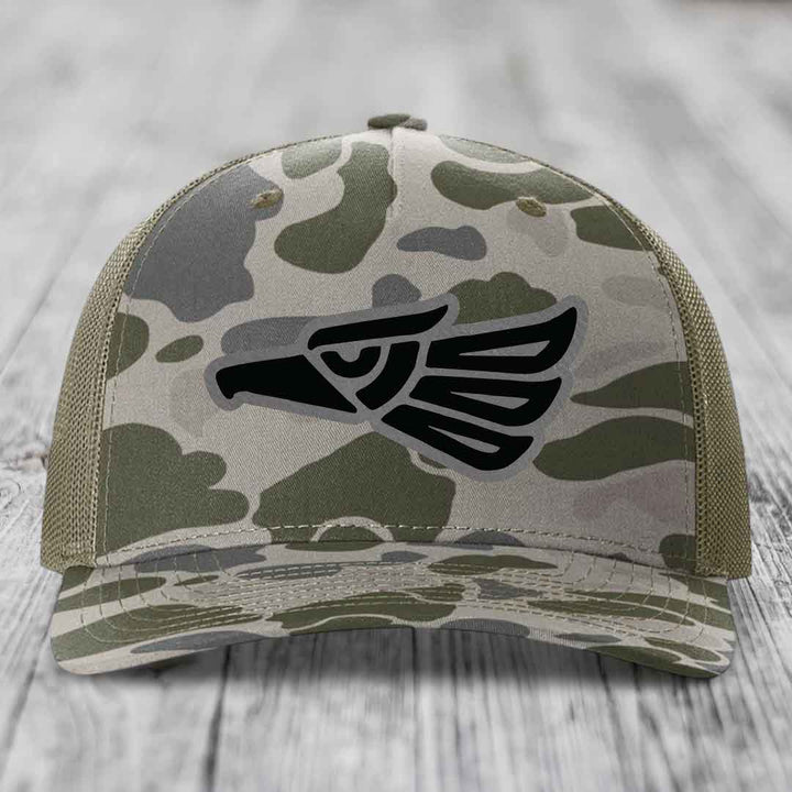 Camouflage trucker hat with black eagle patch on front, olive green mesh back.