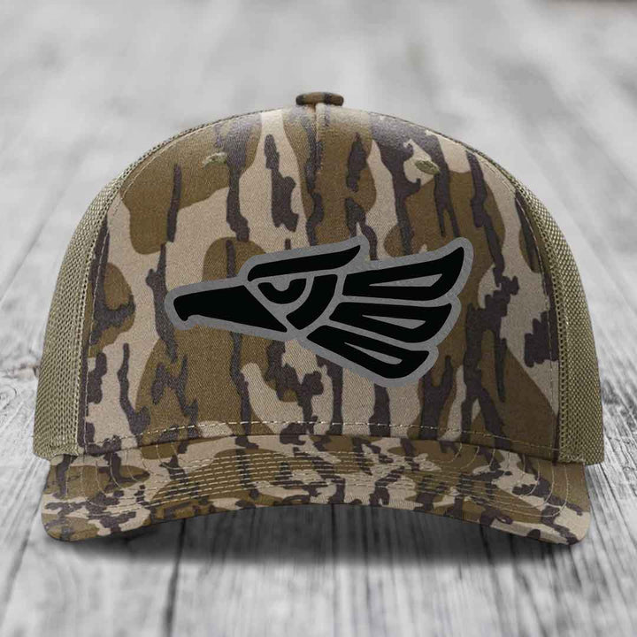 Camouflage trucker hat with black eagle patch on front, sitting on wooden surface.
