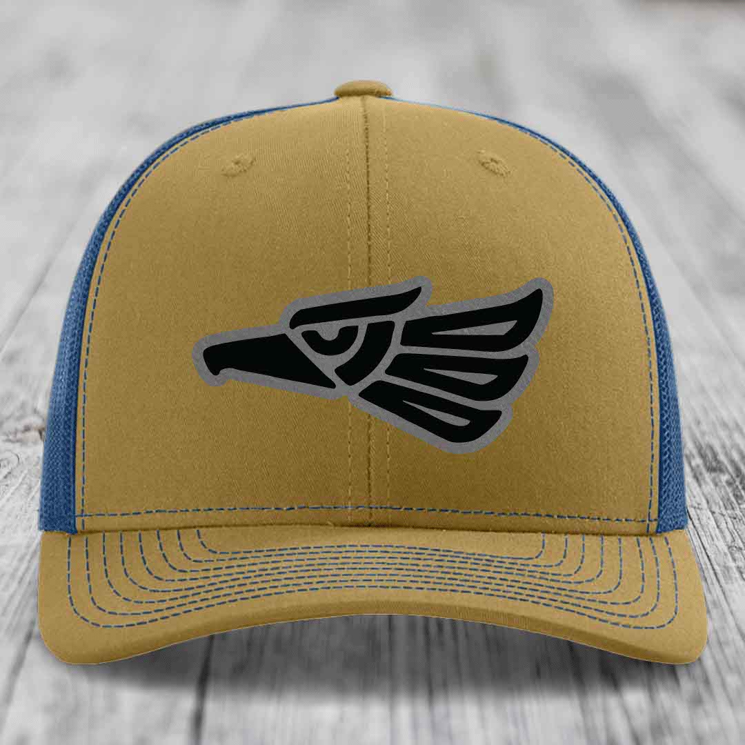 Tan and blue trucker hat with black and gray Aztec eagle patch on front.