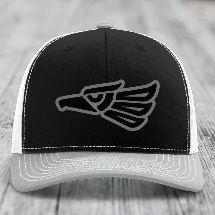 Black and white trucker hat with grey stitching and an Aztec-style eagle patch on front.