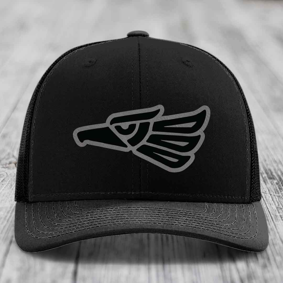 Black trucker hat with embroidered Aztec-style eagle patch on front.