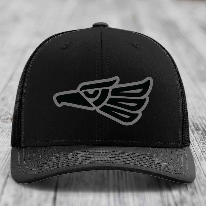 Black trucker hat with embroidered Aztec-style eagle patch on front.