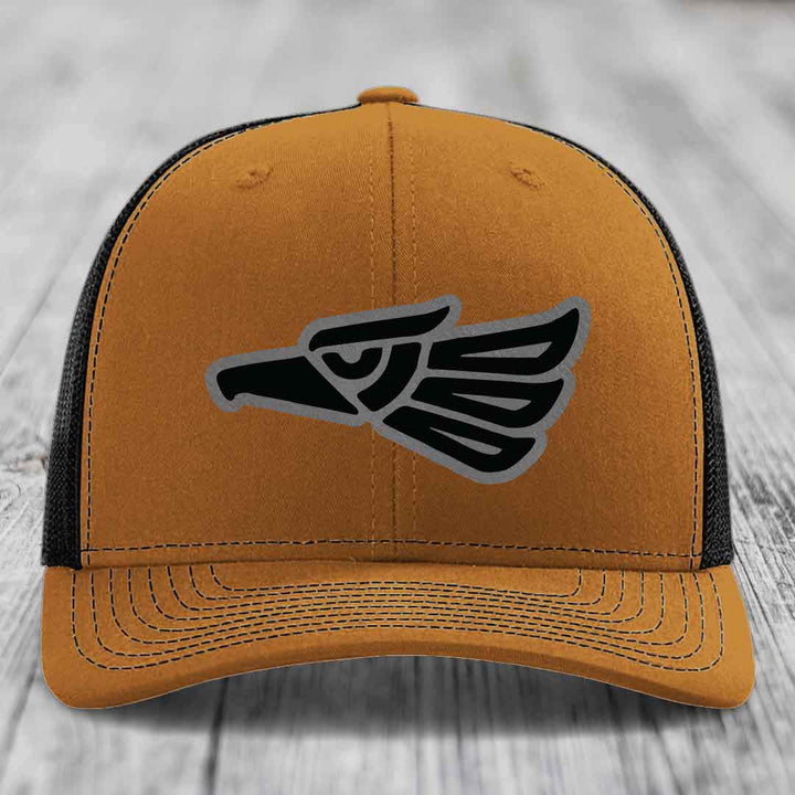 Tan trucker hat with black and grey eagle patch on front, black mesh back.