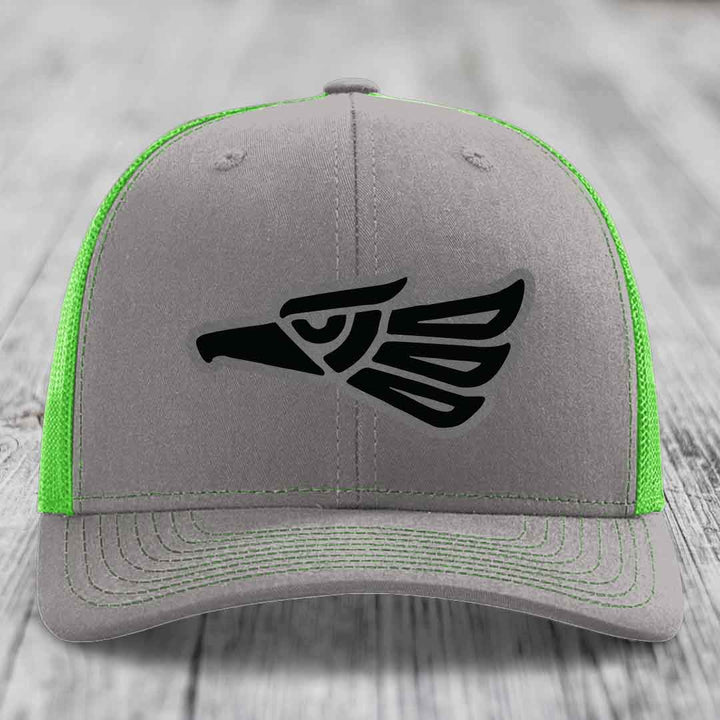Grey trucker hat with neon green mesh and stitching, featuring a black Aztec-style eagle patch on front.