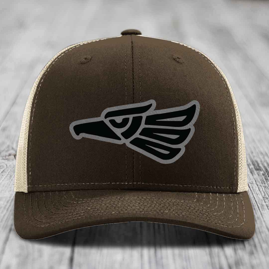 Brown trucker hat with black and grey eagle patch on front, cream mesh back.