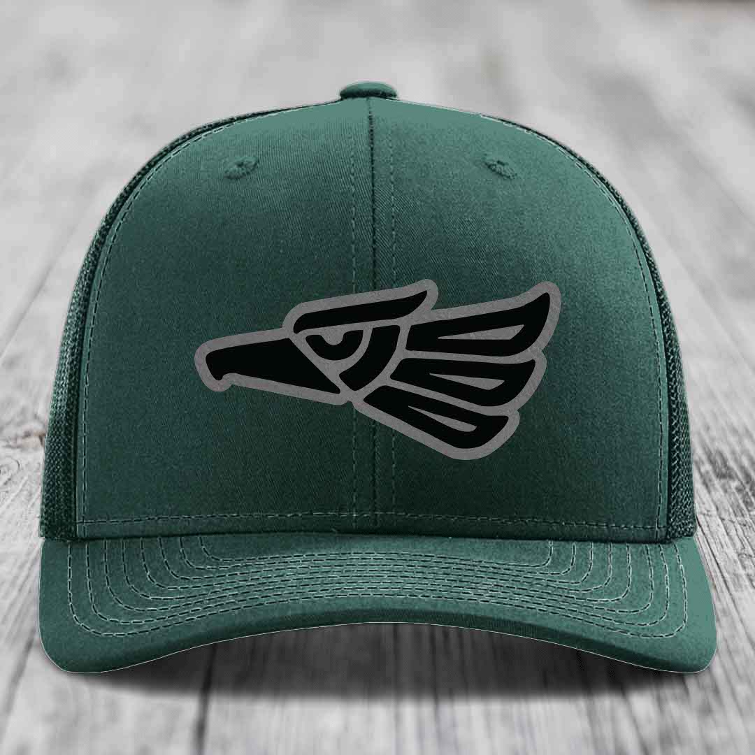 Green trucker hat with black and grey Aztec-style eagle patch on front.