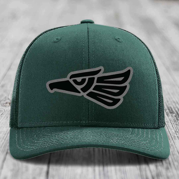 Green trucker hat with black and grey Aztec-style eagle patch on front.
