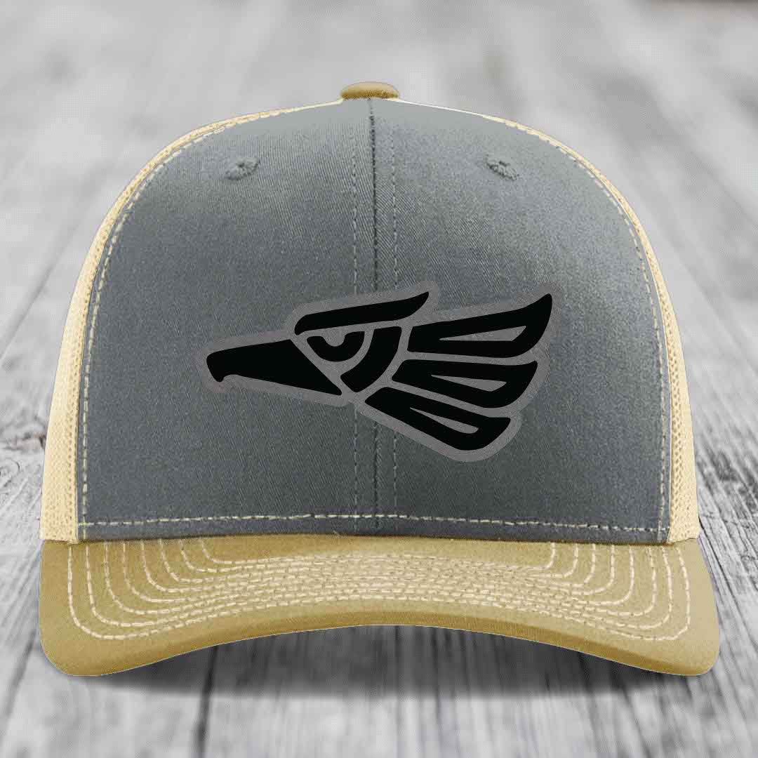 Grey and beige trucker hat with black Aztec eagle leather patch on front.