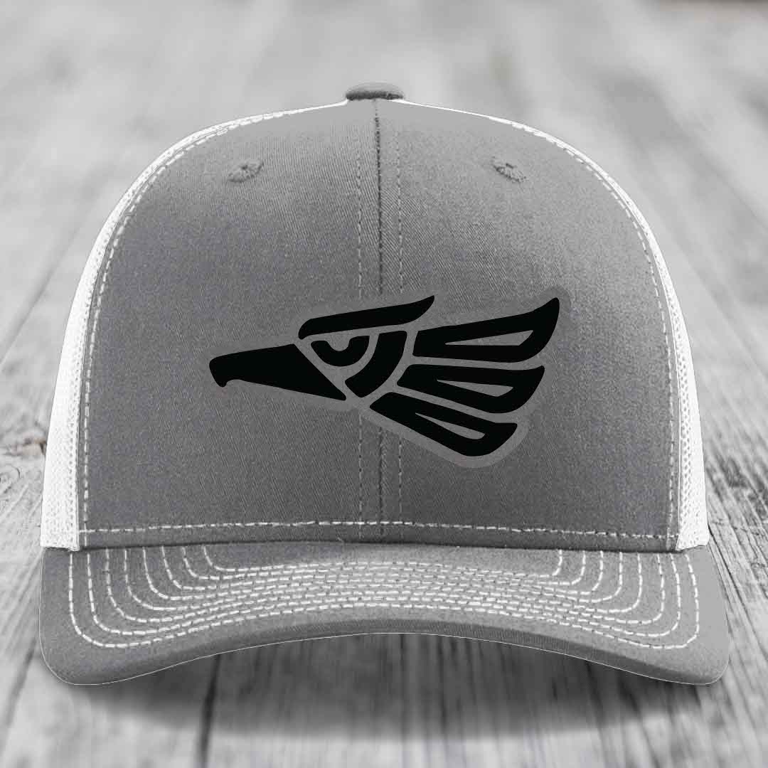 Grey trucker hat with black Aztec-style eagle patch on front, white mesh back and white stitching.