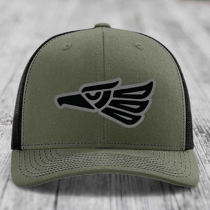 Olive green trucker hat with black and grey Aztec eagle patch on front.