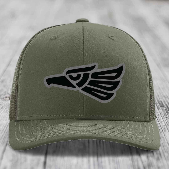 Olive green trucker hat with black and grey Aztec eagle patch on front.