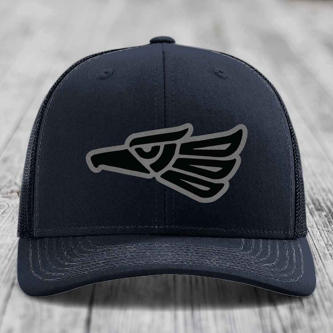 Black trucker hat with embroidered Aztec-style eagle patch on front.