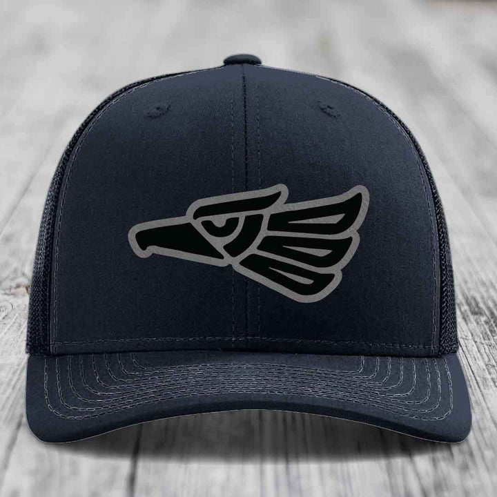 Black trucker hat with embroidered Aztec-style eagle patch on front.