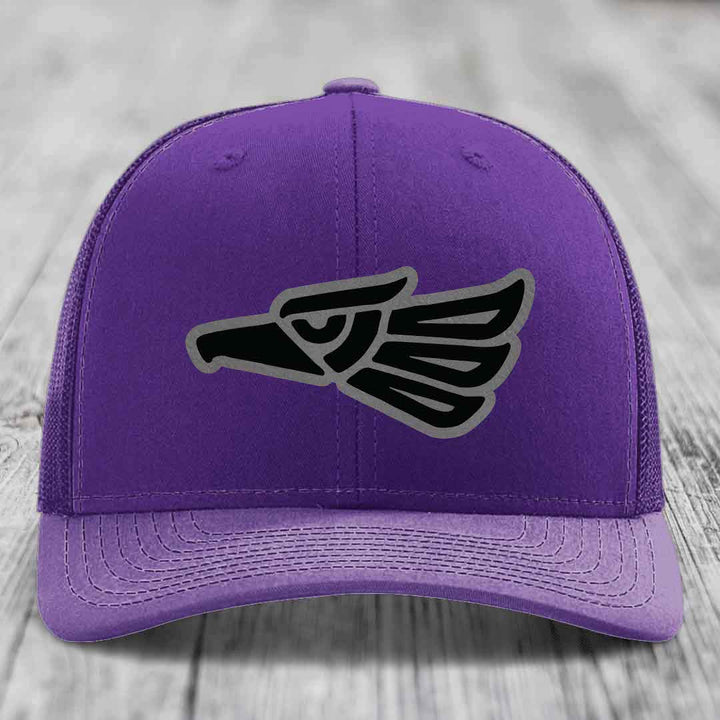 Purple trucker hat with black and grey Aztec eagle patch on front.