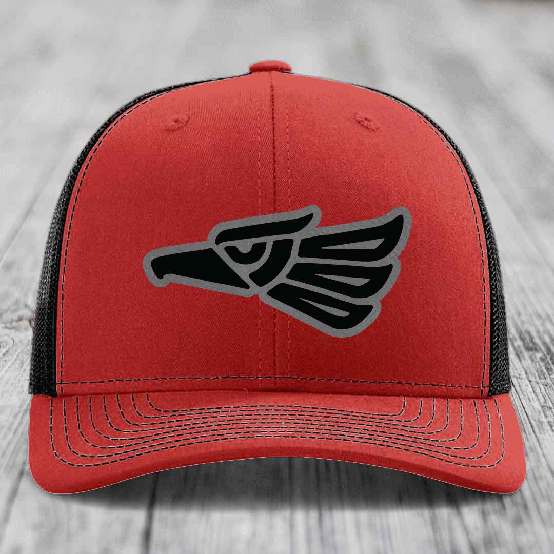 Red trucker hat with black and grey Aztec eagle patch on front.