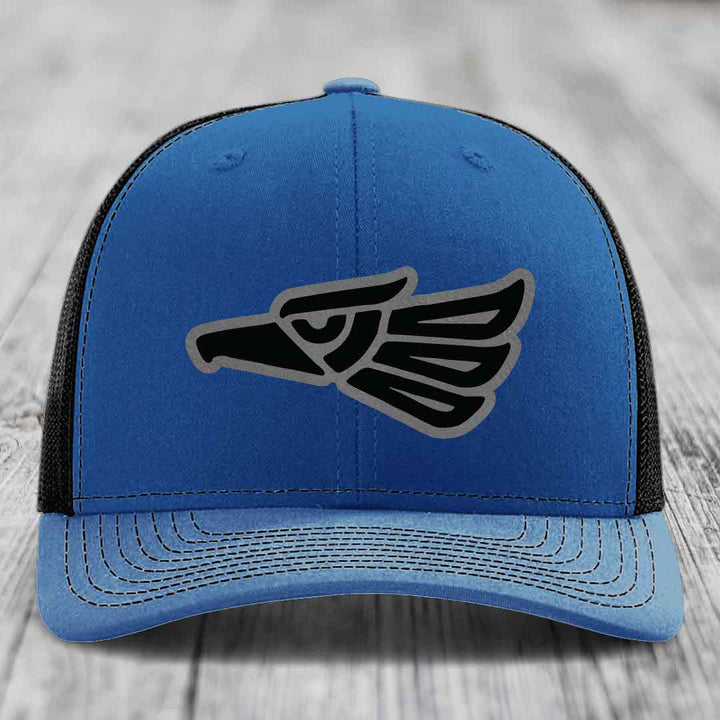 Blue trucker hat with black and grey eagle patch on front, black mesh back.