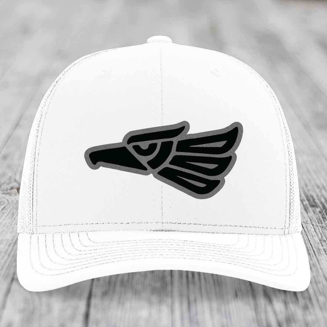 White trucker hat with black and grey Aztec eagle leather patch on front.