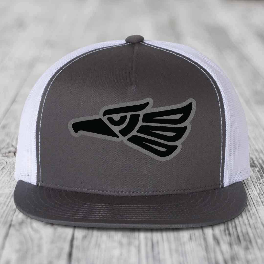 Grey front panel trucker hat with black Aztec eagle patch, white mesh back, and grey brim.
