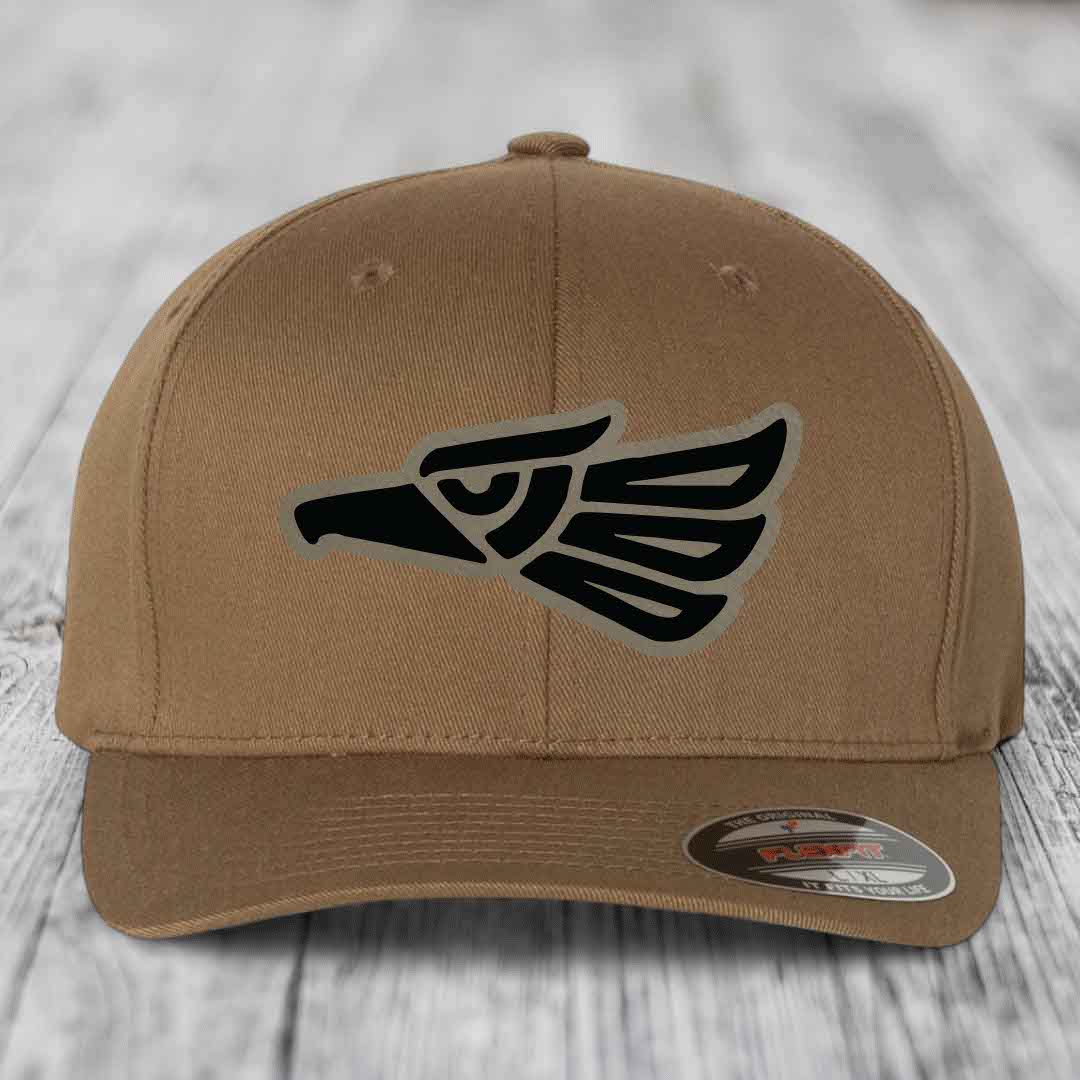 Tan baseball cap with black Aztec-style eagle patch on front, Flexfit brand label visible.