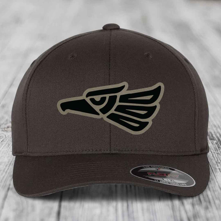 Brown Flexfit hat with Aztec-style eagle patch on front, displayed on wooden surface.