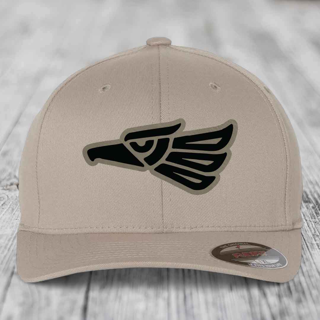 Beige baseball cap with black Aztec-style eagle patch on front, featuring a Flexfit label.