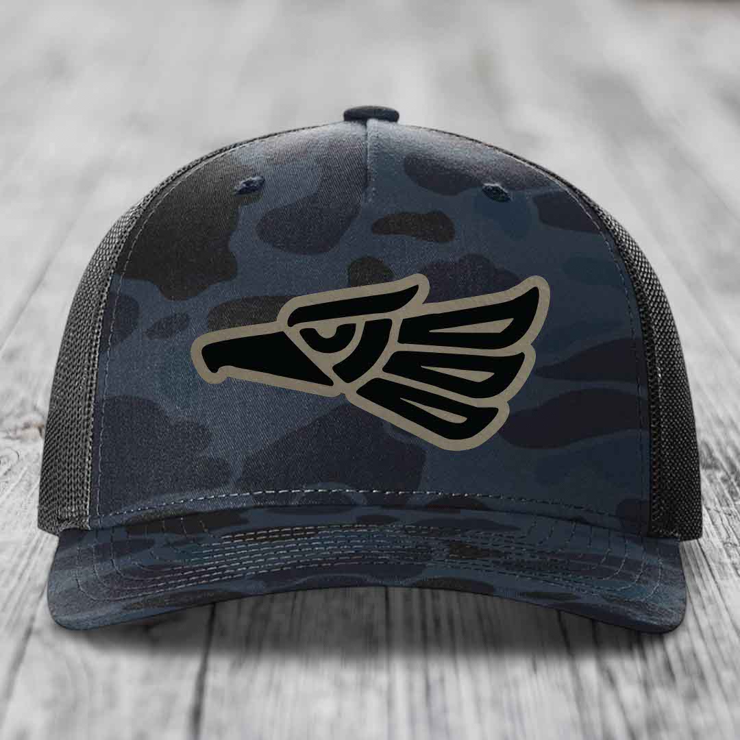 Camouflage trucker hat with Aztec-style eagle patch on front.