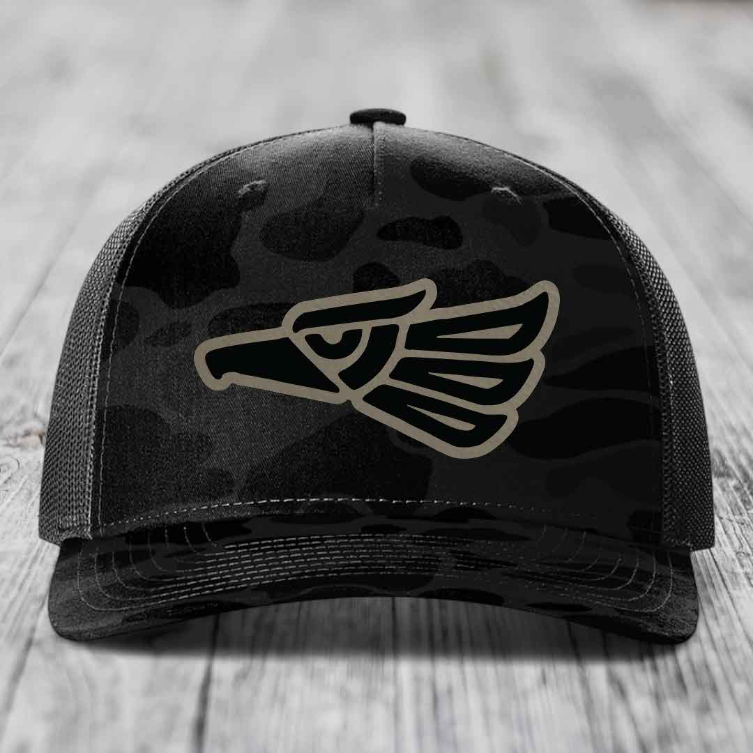 Black camouflage trucker hat with a tan eagle head patch on the front.