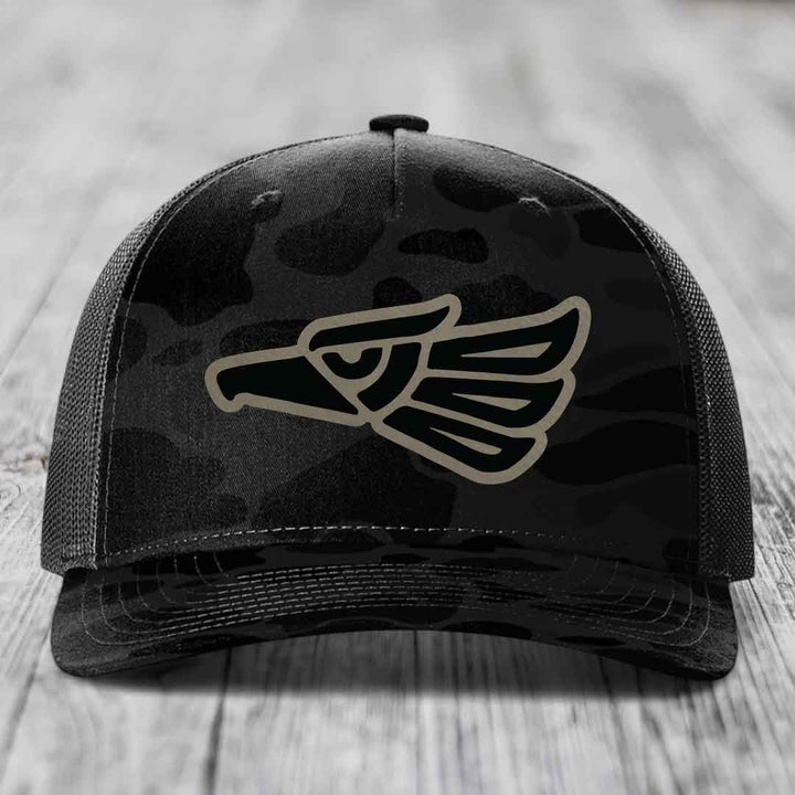 Black camouflage trucker hat with a tan eagle head patch on the front.