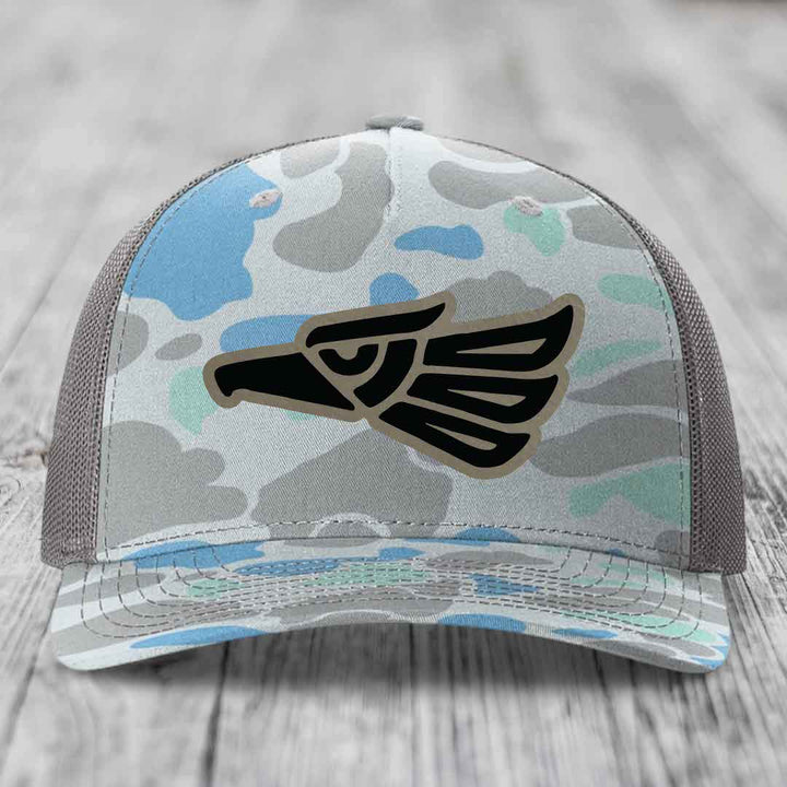 Camouflage trucker hat with black Aztec eagle patch on front, gray mesh back.