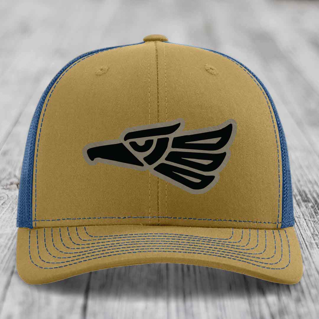 Tan and blue trucker hat with black Aztec eagle patch on front.