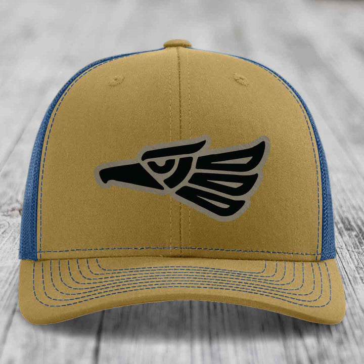 Tan and blue trucker hat with black Aztec eagle patch on front.
