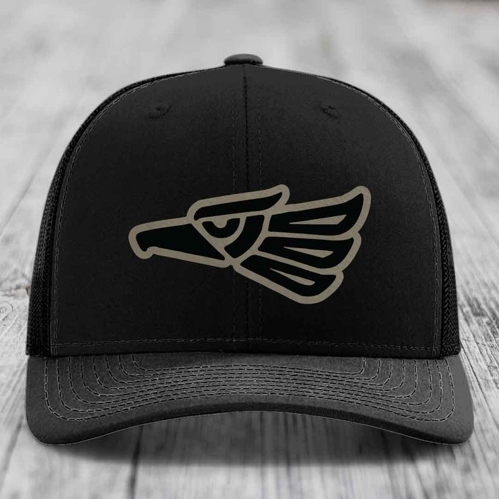 Black trucker hat with embroidered Aztec-style eagle patch on front.