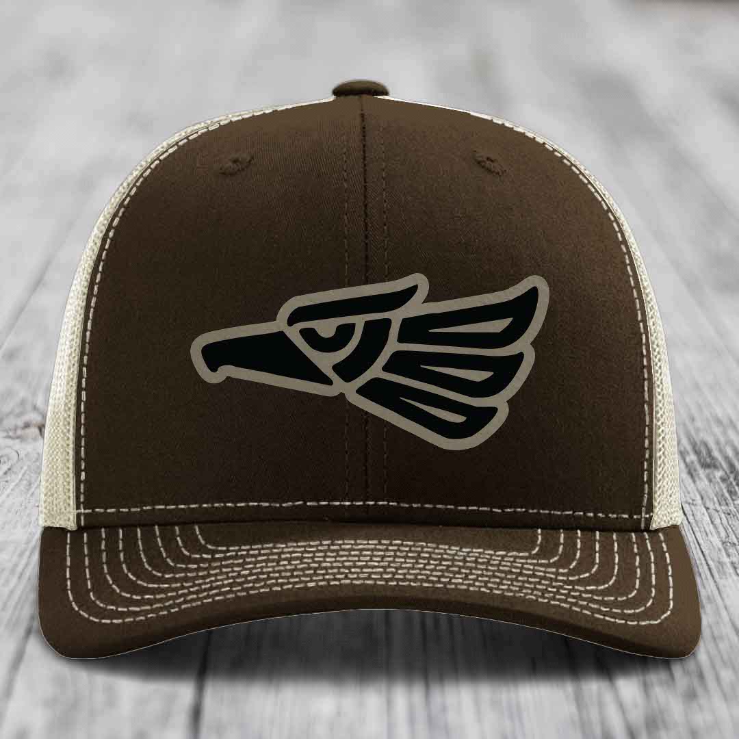 Brown trucker hat with black and tan Aztec eagle patch on front, white stitching details.