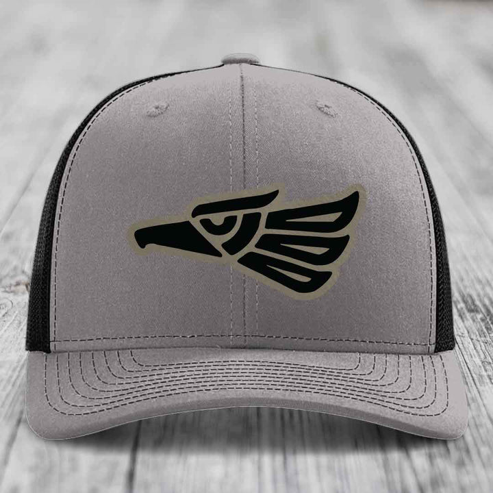 Grey trucker hat with black Aztec-style eagle patch on front, black mesh back.
