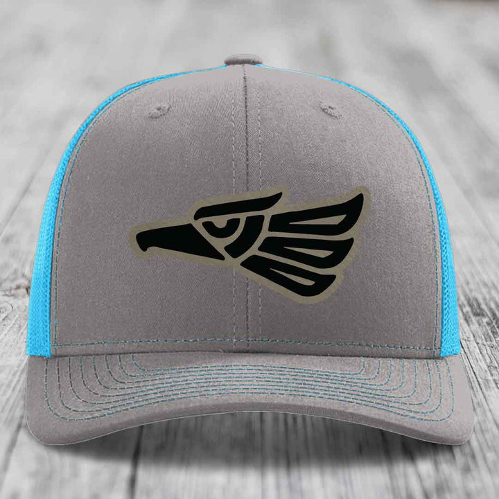 Grey trucker hat with black Aztec eagle patch and blue mesh sides.