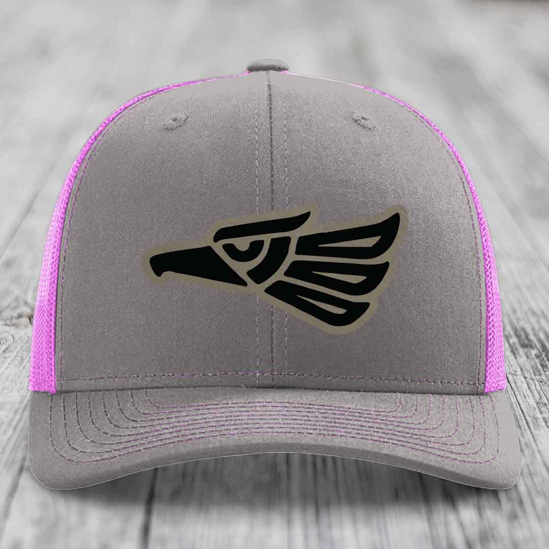 Grey trucker hat with pink mesh sides and a black Aztec-style eagle patch on front.