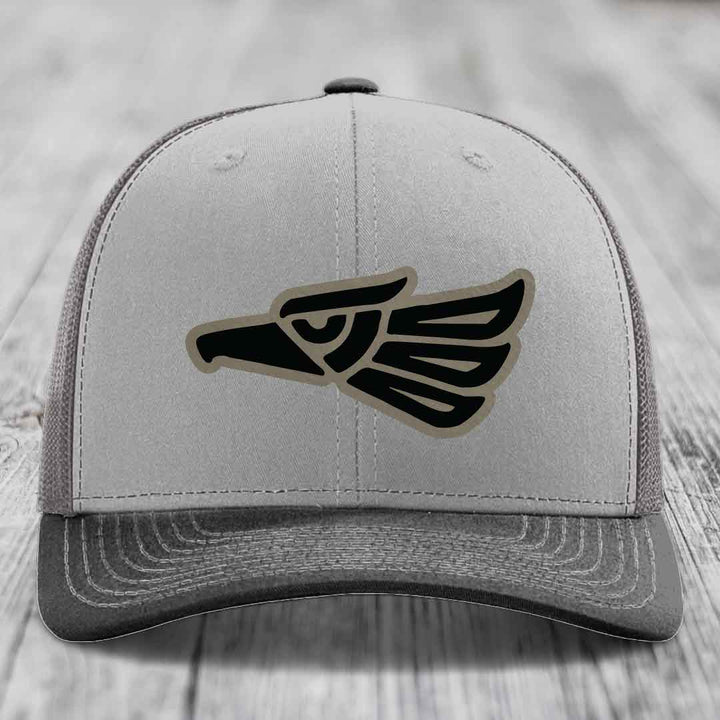 Grey trucker hat with black and tan Aztec eagle patch on front.