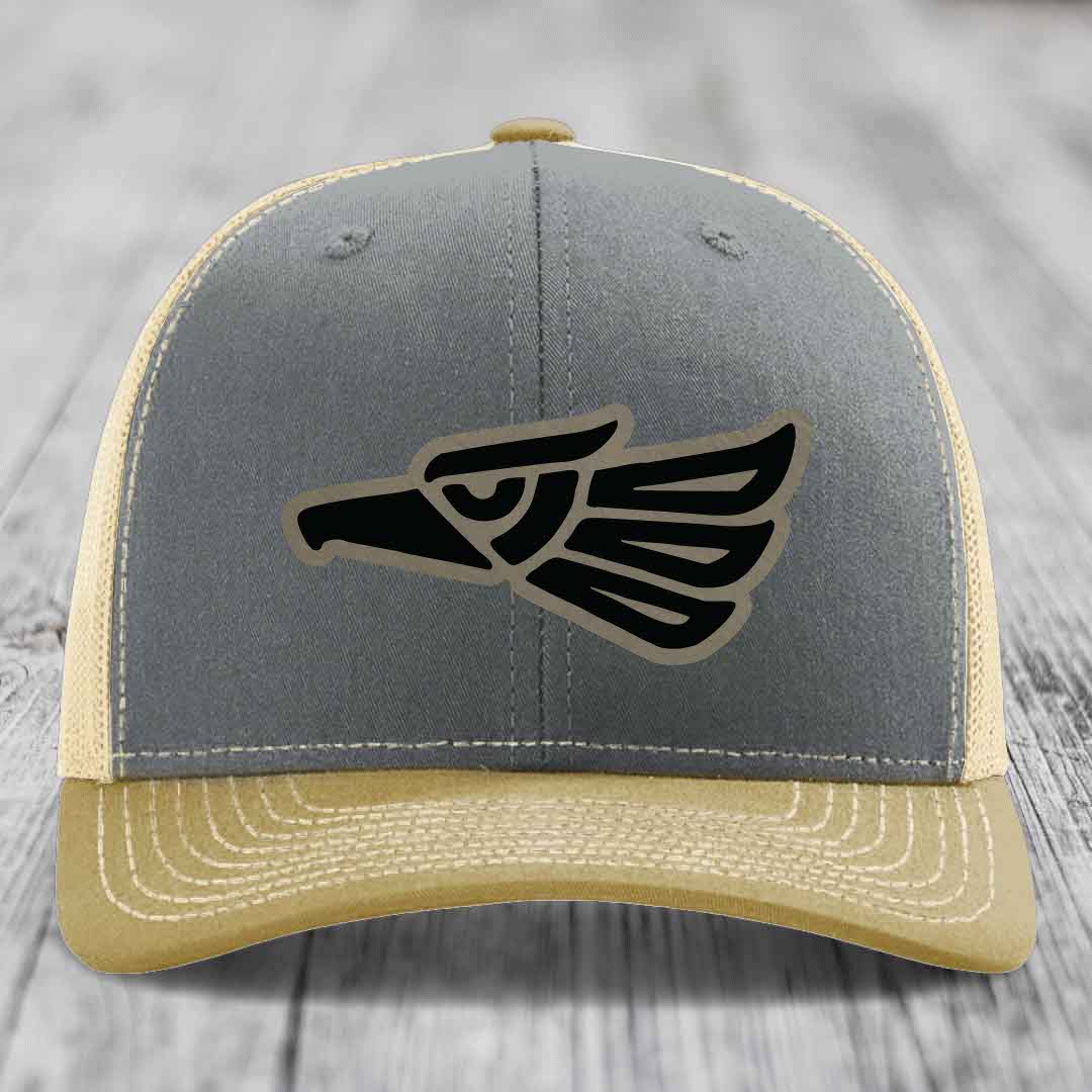 Grey and beige trucker hat with black Aztec eagle leather patch on front.