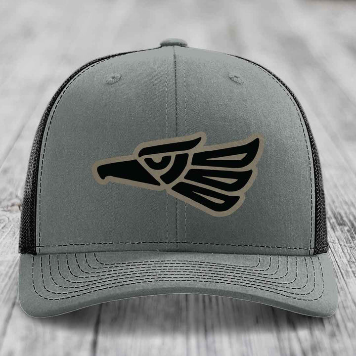 Grey trucker hat with black and tan Aztec eagle patch on front.