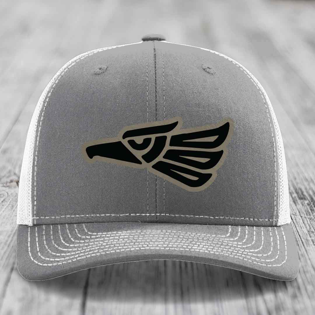 Grey trucker hat with black and tan Aztec eagle patch on front, white mesh back and stitching.