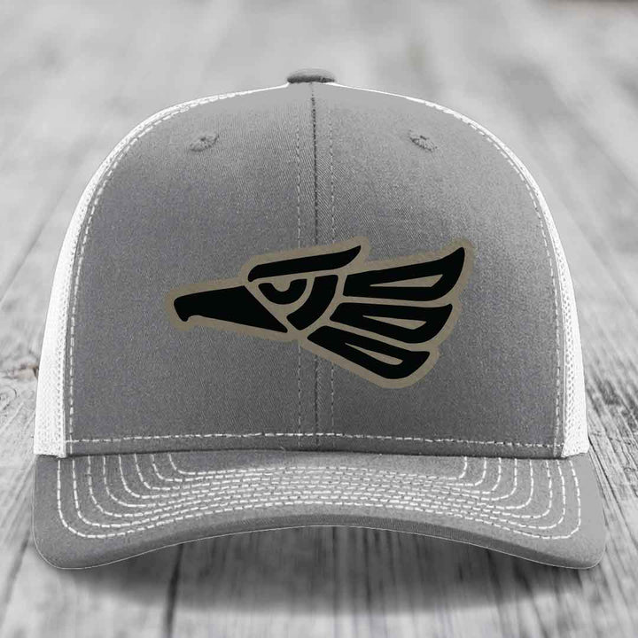 Grey trucker hat with black and tan Aztec eagle patch on front, white mesh back and stitching.