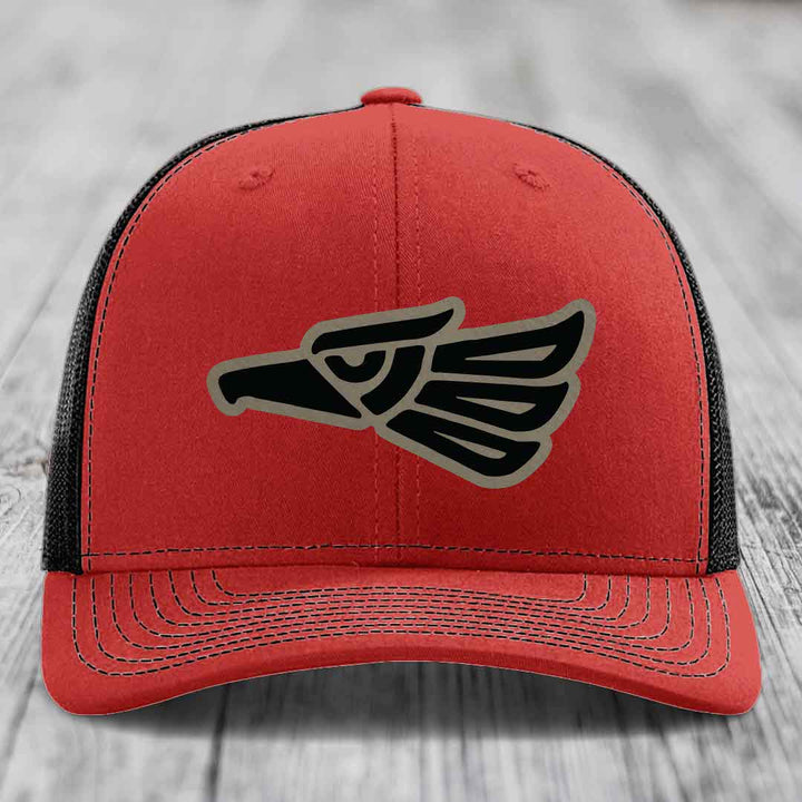 Red trucker hat with black and grey Aztec eagle patch on front.